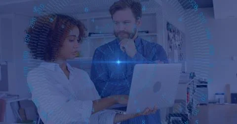 Two professionals analyzing data on laptop in modern office, with blue HUD Stock Photos