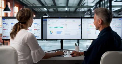 Two Professionals Discuss ERP Software Integration On Desktop Monitors Togeth Stock Photos