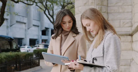 Two professionals review documents in urban setting, Pair of businesswomen 스톡 동영상 322557803