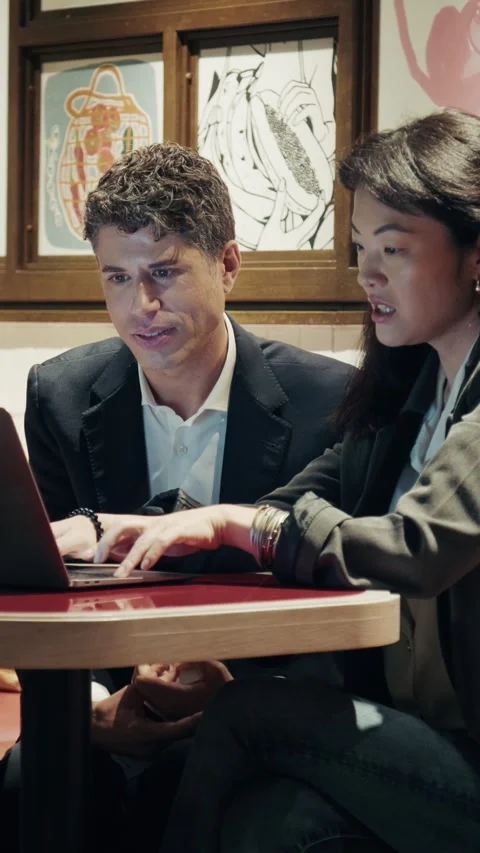 Two professionals seated at a modern cafe working with a laptop Stock-Footage 305982608