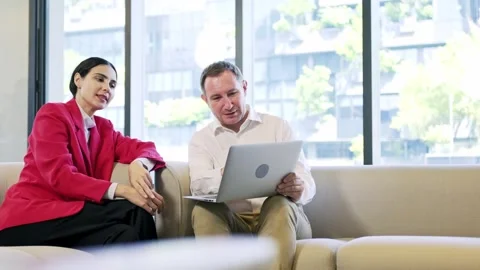 Two professionals sit on a sofa in a bright office, smiling and reviewing a.. Stock-Footage 347061043