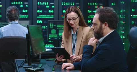 Two programmers work together in server room at desktop: woman holds tablet, man Stock Footage 145297480