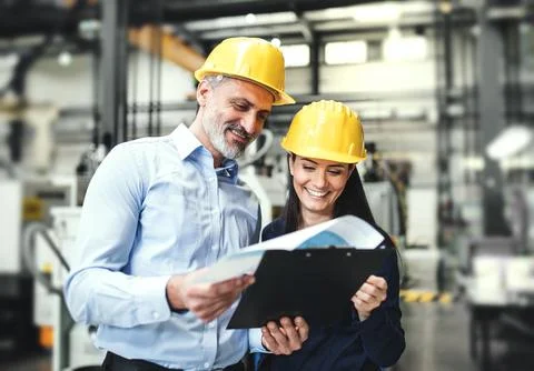 Two project managers standing in modern industrial factory, looking document in Stock Photos