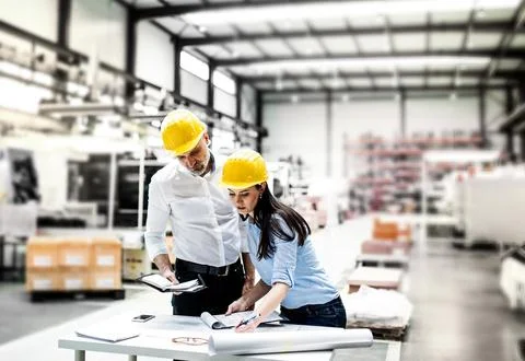 Two project managers standing in modern industrial factory, looking blueprints Stockfoto's