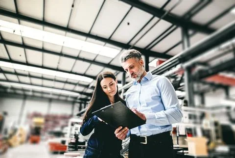 Two project managers standing in modern industrial factory, looking document in Stockfoto's