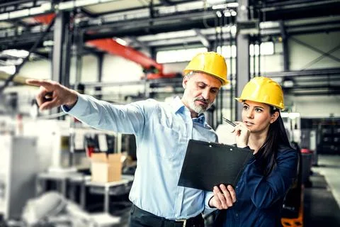 Two project managers standing in modern industrial factory, looking document in Stock Photos