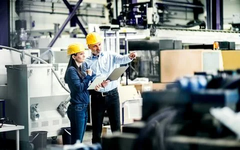 Two project managers standing in modern industrial factory, looking document in Stock Photos