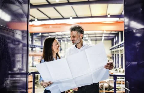 Two project managers standing in modern industrial factory, looking blueprints 스톡 사진