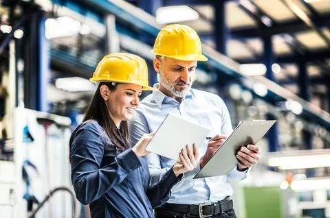 Two project managers standing in modern industrial factory, looking document in Stockfoto's