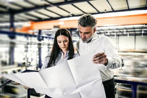 Two project managers standing in modern industrial factory, looking blueprints Stock Photos