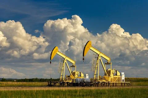 Two pumpjacks in a field with storm clouds and blue sky in the background with w Stock Photos