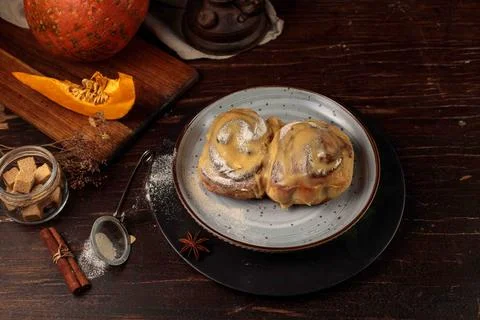 Two pumpkin cinnabons with icing on a black plate. On a dark wooden table, with Stock Photos