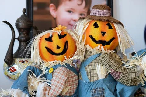 Two pumpkin head scarecrow on display next to a babys portrait Stockfoto's