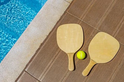 Two rackets and a ball next to the swimming poll Stock Photos