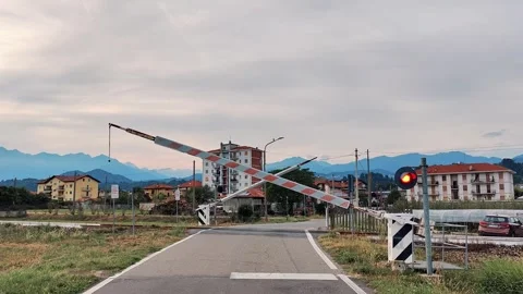 Two railway barriers simultaneously lowering at crossing with view of urban Stock Footage 324845413