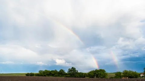 Two rainbows over trees and agricultural fields with cloudy sky in background Stock Photos