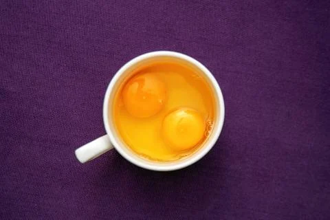 Two raw chicken eggs cracked into a glass on a table, fresh and ready for c.. Stock Photos
