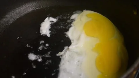 Two raw eggs, freshly cracked into a large black skillet cooking slowly. Video stock 339100969