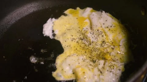 Two raw eggs, freshly cracked into a large black skillet cooking slowly. Video stock 339100971