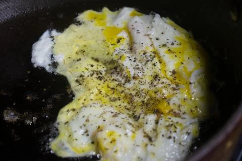 Two raw eggs, freshly cracked into a large black skillet cooking slowly. Stock Photos