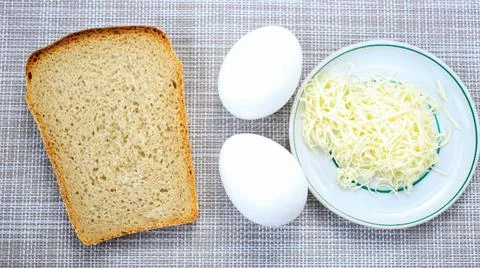 Two raw eggs next to a cut piece of bread and grated cheese. Foto stock