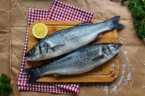 Two raw fish on a cutting Board decorated with a lemon slice close-up.Textu.. Stock Photos