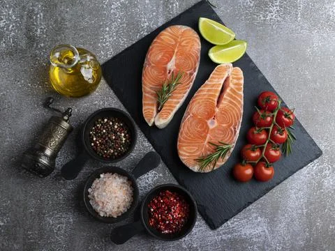 Two raw fresh steak fish trout, salmon and spices on black stone surface Stock Photos