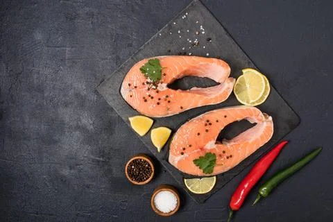 Two raw salmon steaks on a stone board with black pepper, salt, lemon slice.. Stock Photos