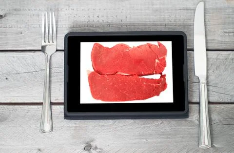 Two raw steaks on a tablet screen with a fork and a knife Stock Photos