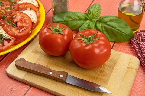 Two raw tomatoes and sprigs of fresh basil on a table Stock Photos