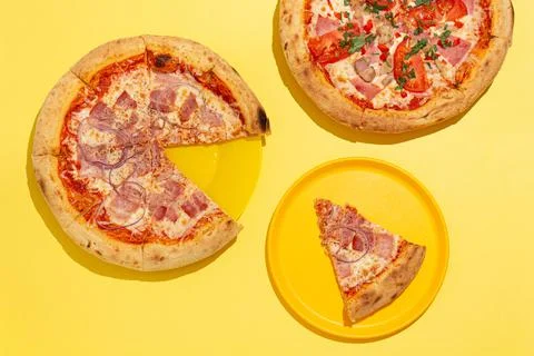 Two ready-made pizzas and one slice on a yellow background Foto stock
