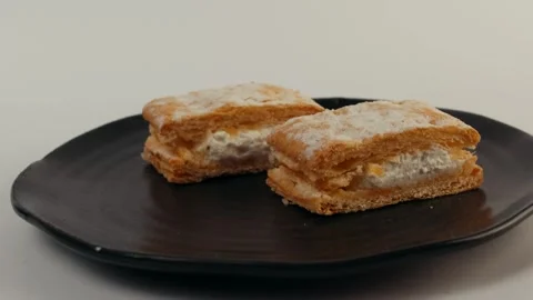 Two rectangular cream pastries sit on a matte black plate. Each features golden Video stock 309639551