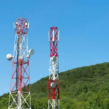 Two red and white radio towers with forest and sky in background Stock Photos