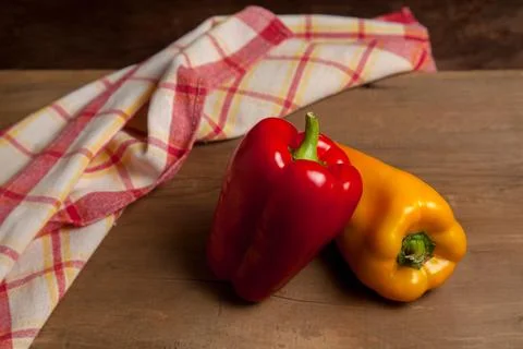 Two red and yellow bell pepper on wooden background with red kitchen towel. . Stock Photos