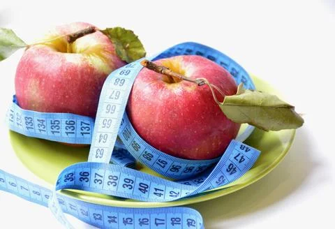 Two red apples and a flexible centimeter on a green plate on a white background Stock Photos