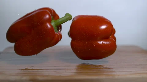 Two red bell peppers are dropped onto a cutting board in slow motion and bounce Stock Footage 64577854
