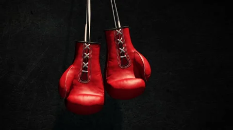 Two Red Boxing Gloves Hang Against a Dark Background. Stock Footage 43730538
