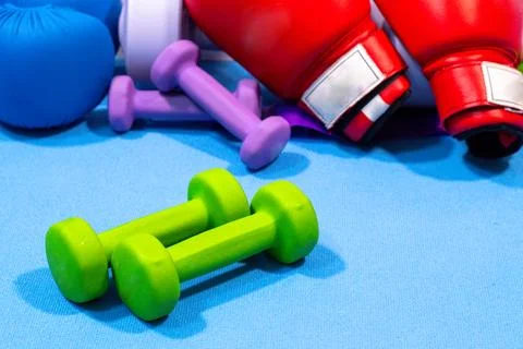 Two red boxing gloves placed prominently among colorful dumbbells Stock Photos