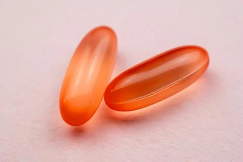 Two red capsules on a pink background. Focus on foreground, soft bokeh. Stock Photos