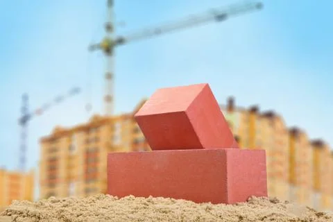 Two red ceramic bricks on the sand at the building background with crane Stock Photos