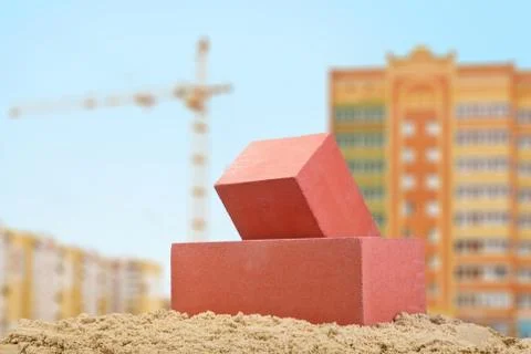 Two red ceramic bricks on the sand at the building background with crane Stock Photos