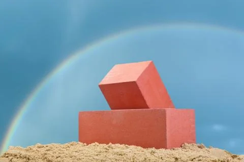 Two red ceramic bricks on the sand at the dark blue sky background with rainb Stock Photos