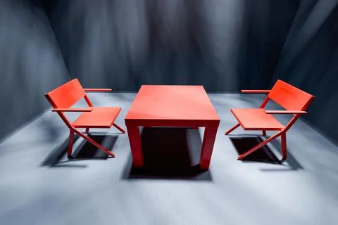 Two red chairs and table in spotlight in empty dark interrogation room Stock Photos