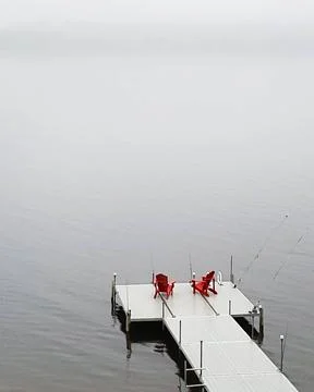 Two red chairs on a dock overlooking a foggy lake at dawn in a serene fishi.. Stock Photos