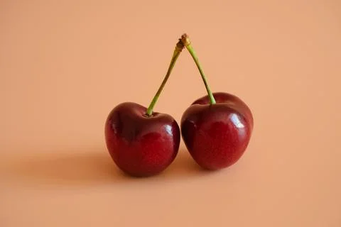 Two red cherries on a peach background Stock Photos