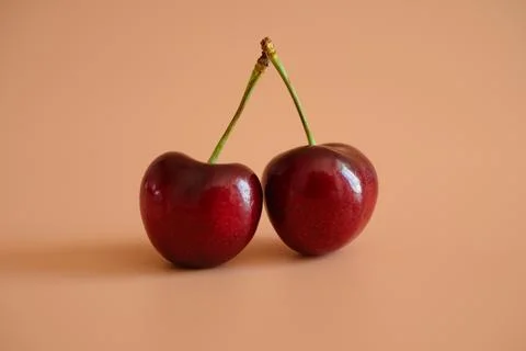 Two red cherries on peach background Stock Photos