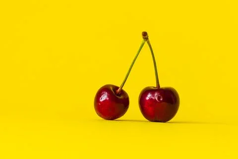 Two red cherries stand exactly on a bright yellow summer background. Stock Photos