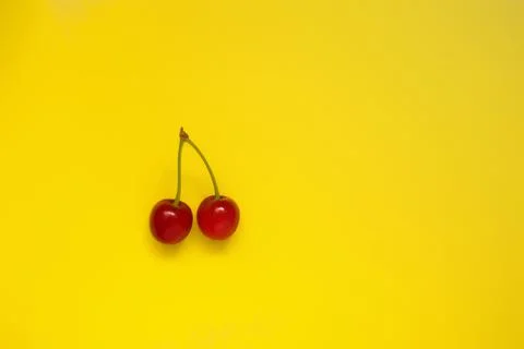Two red cherries on a yellow background, top view, natural product. Stock Photos