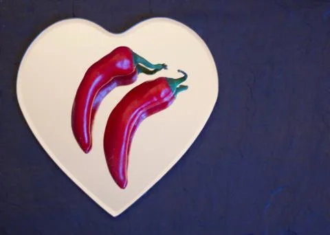 Two red chilli peppers lying side by side on a heart Stock Photos