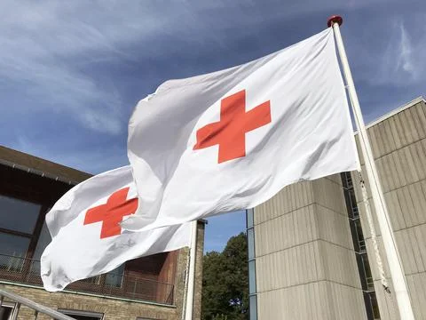Two Red Cross flags waving in the wind against a blue sky. Close up photo. Stock Photos